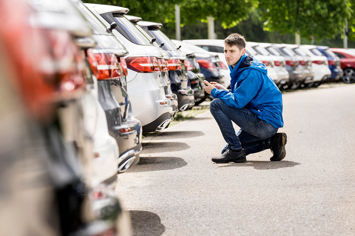 Mitarbeiter eines Autohauses mit iPad kniend vor abgestellten Autos, die zum Verkauf stehen