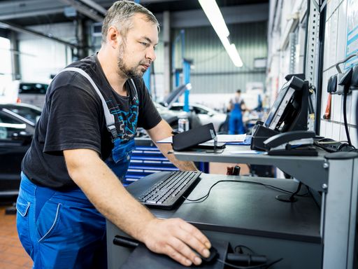 Kfz-Mechatroniker in Werkstatt steht vor Werkstattwagen mit PC