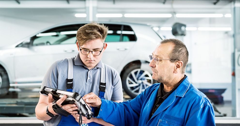 Zwei Personen stehen in einer Werkstatt und bedienen ein Tablet zur Diagnose von Autos.