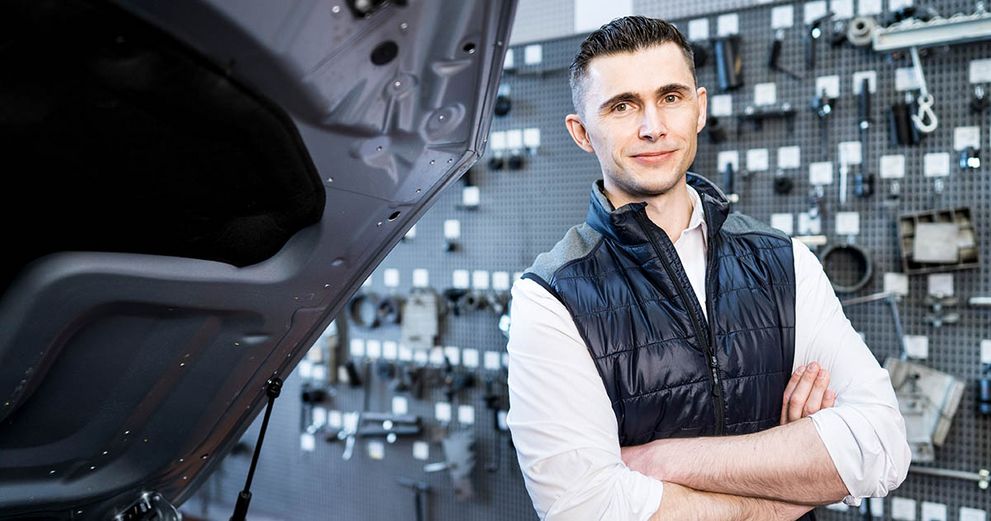 Person steht vor einem Auto in einer Werkstatt mit aufgeklappter Motorhaube.