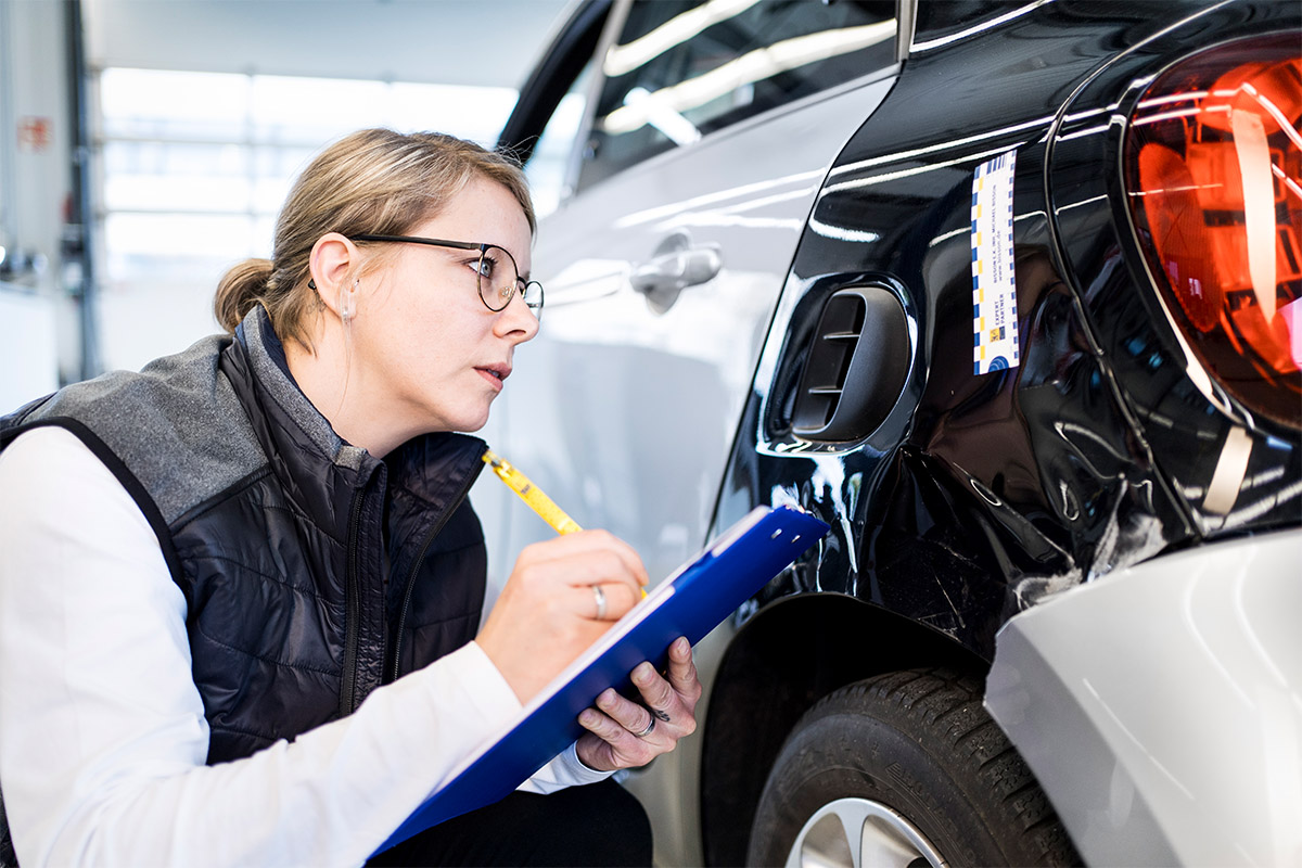 Kfz-Sachverständige betrachtet den Schaden en einem Kotflügel und macht sich Notizen.