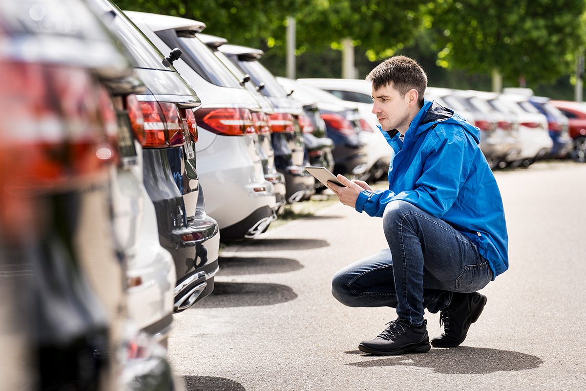 Fuhrparkmanager begutachtet in Reihe abgestellte Autos seines Firmen-Fuhrparks. Am Tablett kann er sich direkt in seine Fuhrparkmanagement-Software einloggen.