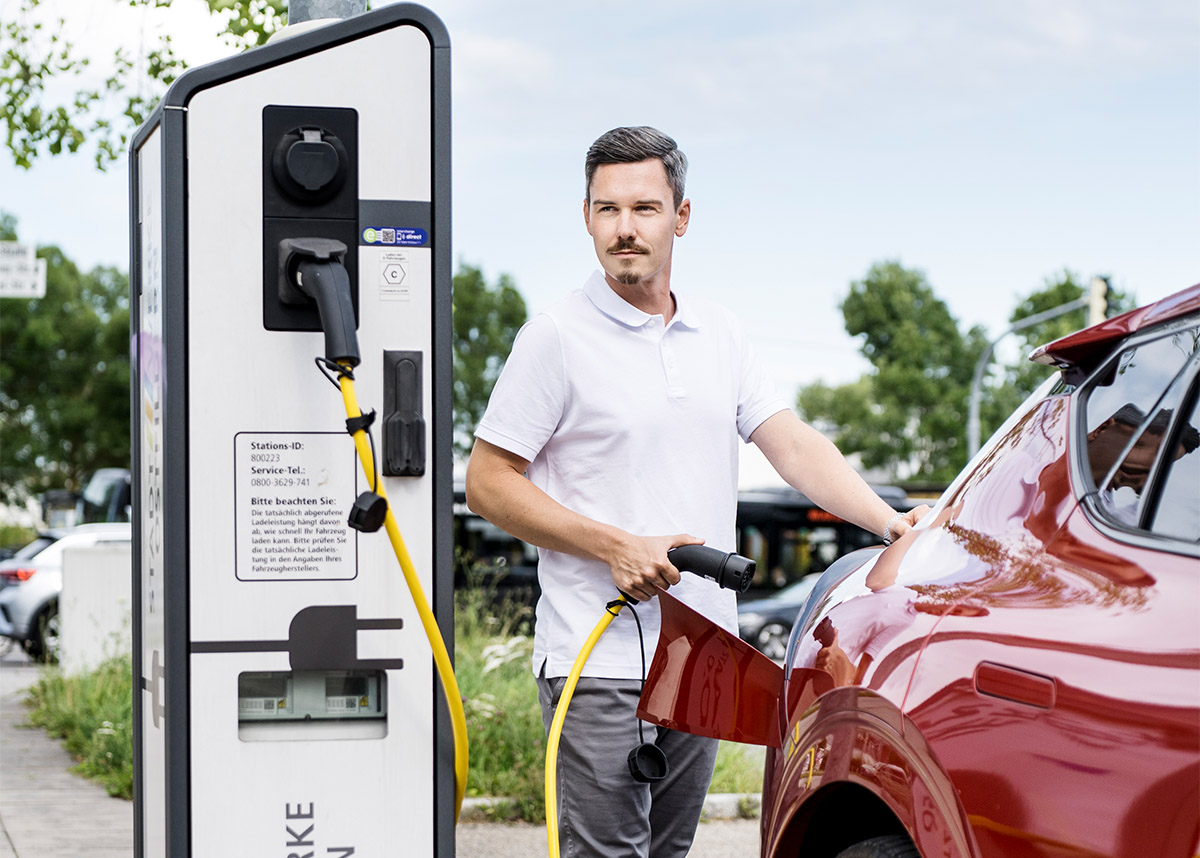 Person steht an einer Ladesäule für Elektroautos und lädt ein E-Auto.
