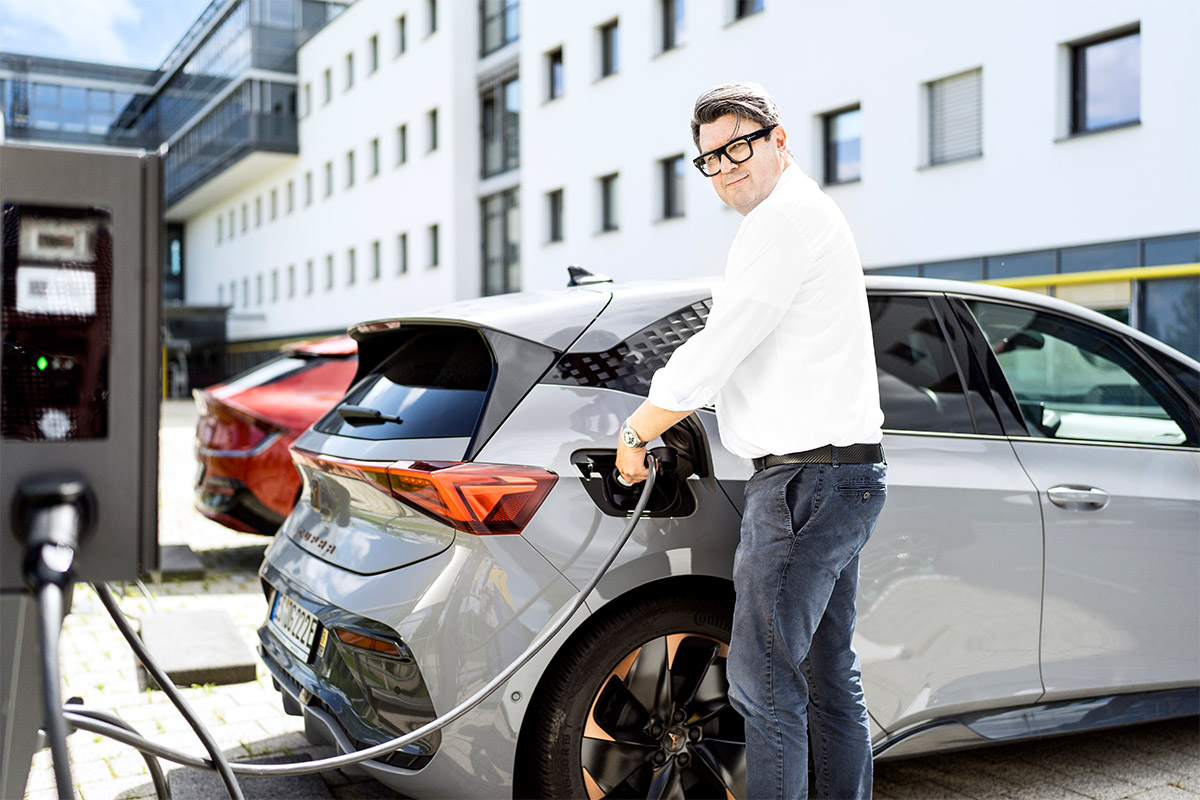 Person steht an einer E-Ladesäule und lädt sein Elektrofahrzeug.