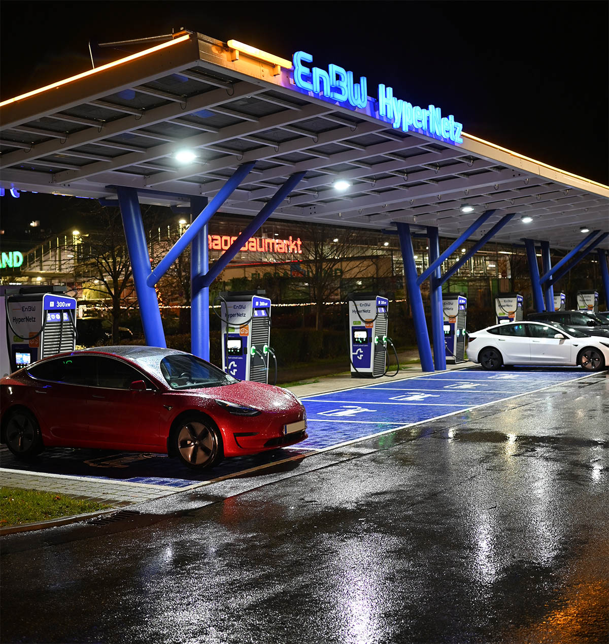 E-Autos nachts an einem Ladepark mit Schnell-Lader, daneben noch freie Ladeplätze